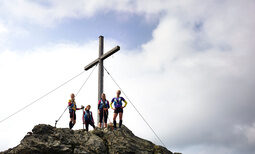 Eine Gruppe blickt nach geschafften Aufstieg vom Gipfelkreuz herunter.