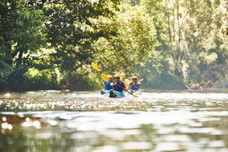 Zwei Kajakfahrer frontal fotografiert, paddeln auf einem ruhigen Fluss im Bayerischen Wald, umgeben von Bäumen.