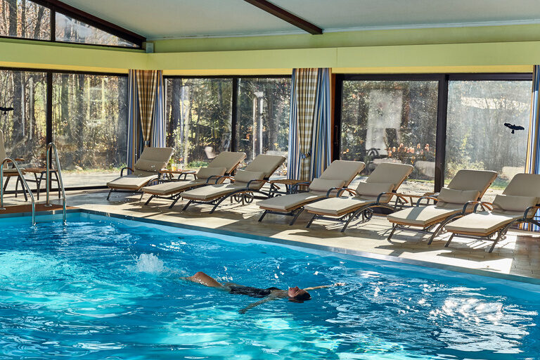 Eine Besucher des Hotels Das Bayerwald schwimmt im Innenpool auf dem Rücken.