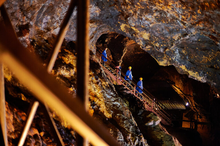 Besucher steigen auf einer Holztreppe durch das beleuchtete Silberbergwerk Bodenmais im Bayerischen Wald.