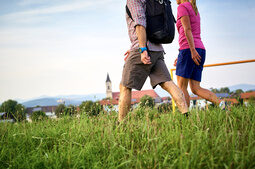 Zwei Personen spazieren mit Rucksäcken durch die weite Graslandschaft im Bayerischen Wald.